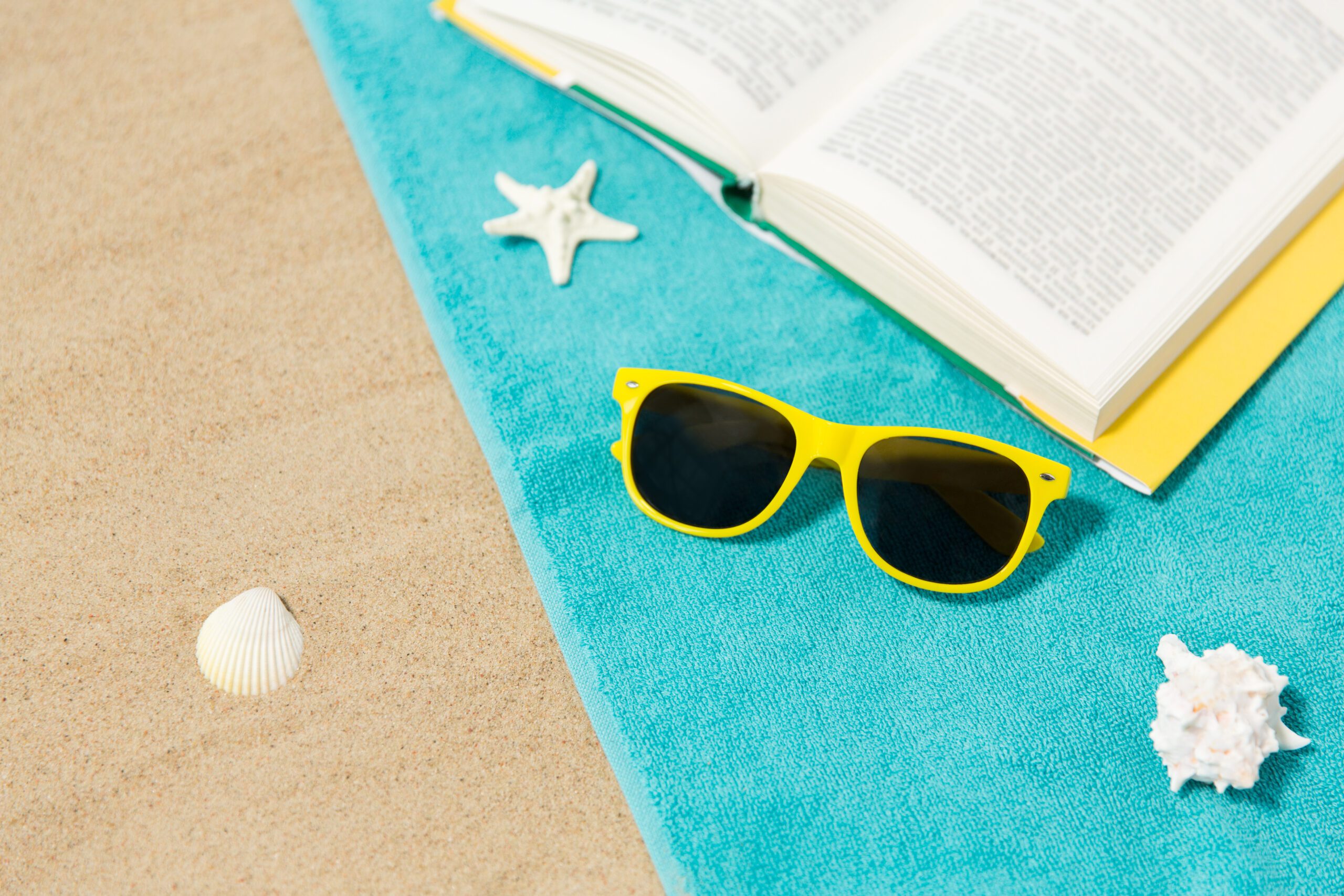 sunglasses and book on beach towel on sand