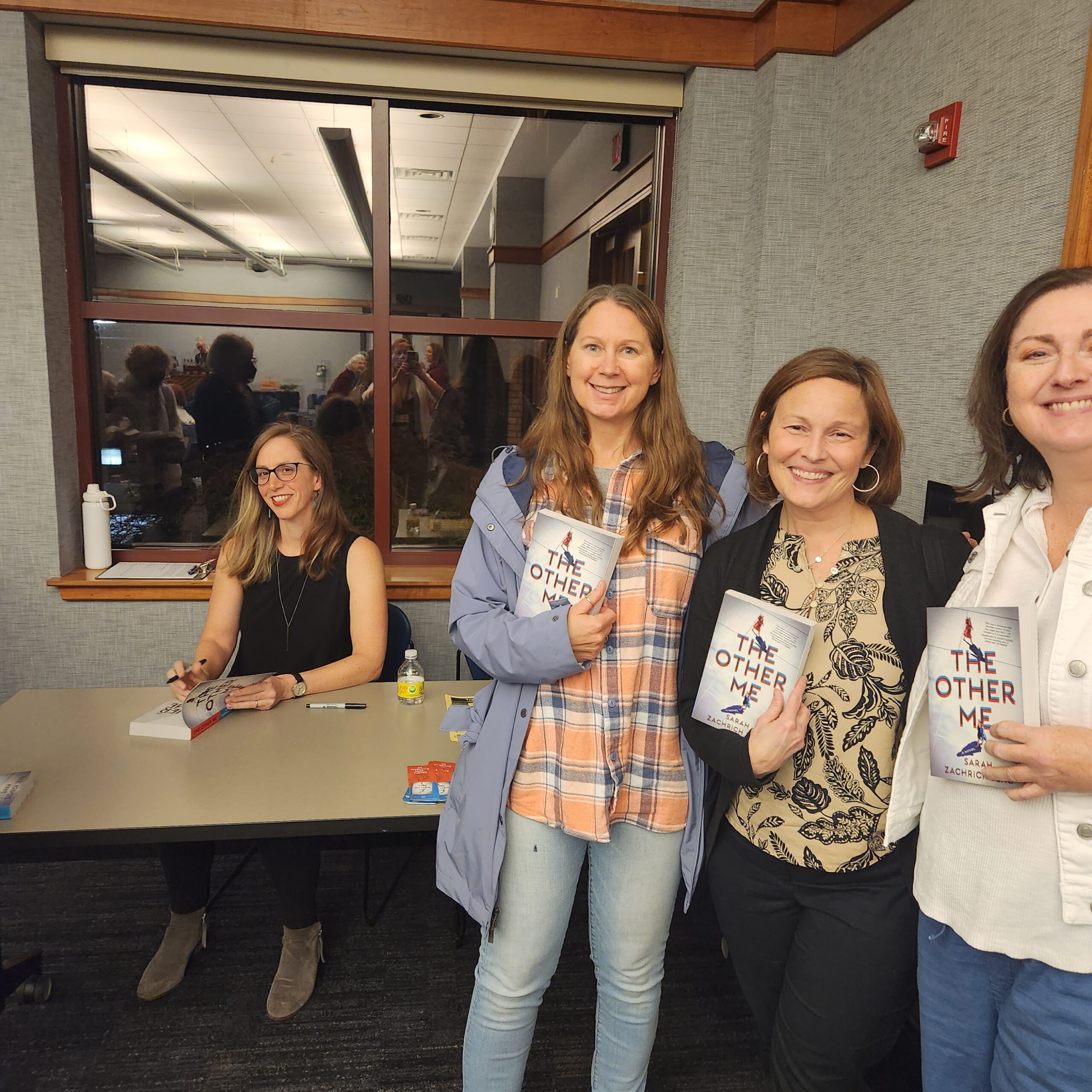 Adults hold copies of book The Other Me while the author signs another copy