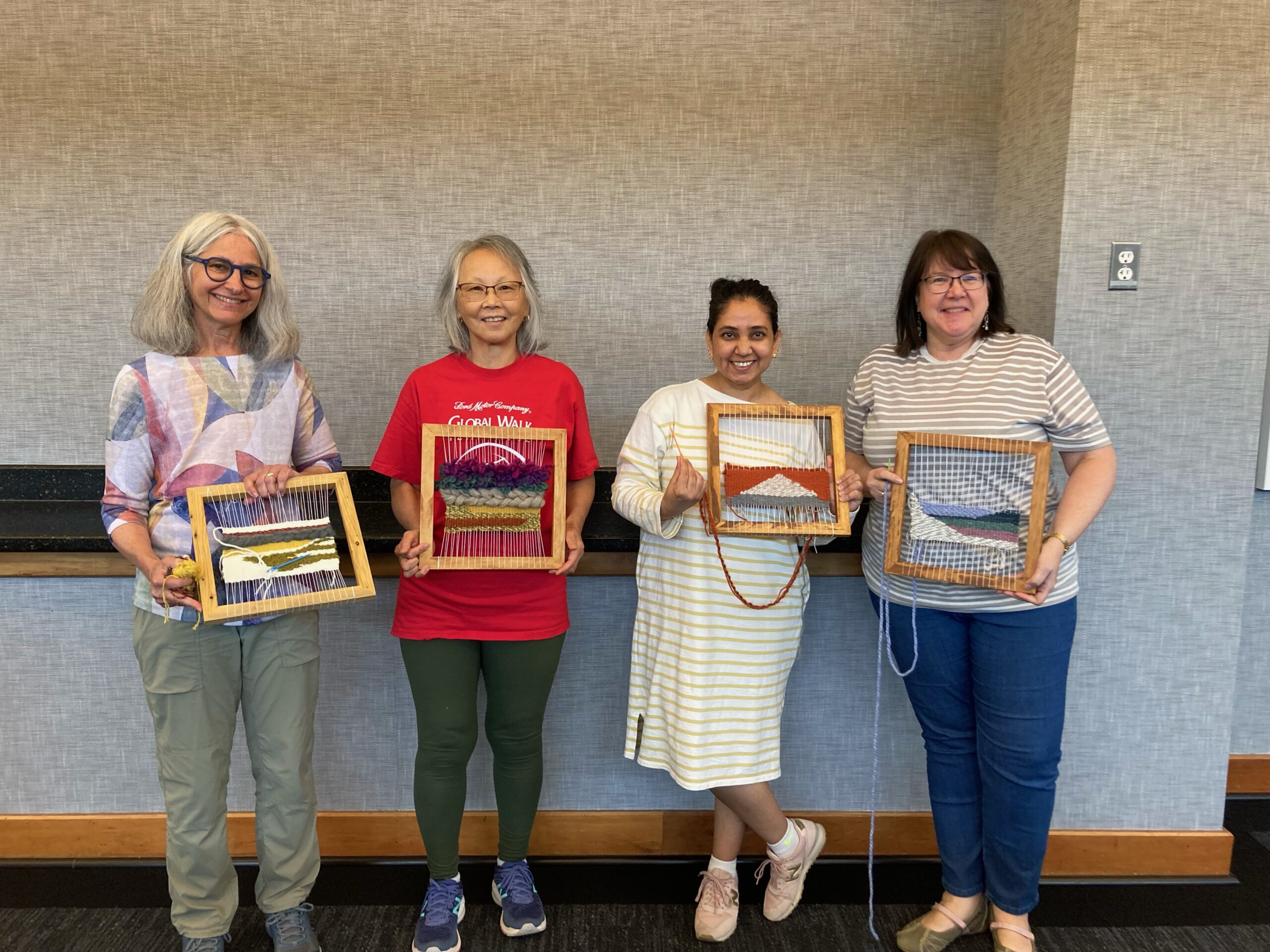 Adults hold tapestry creations in the Main Library meeting room