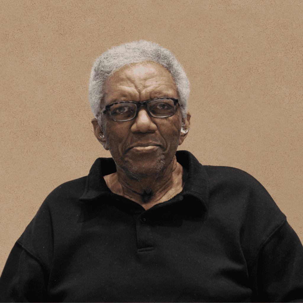 Portrait of a Black man with short grey hair wearing a polo shirt and reading glasses, smiling at the camera