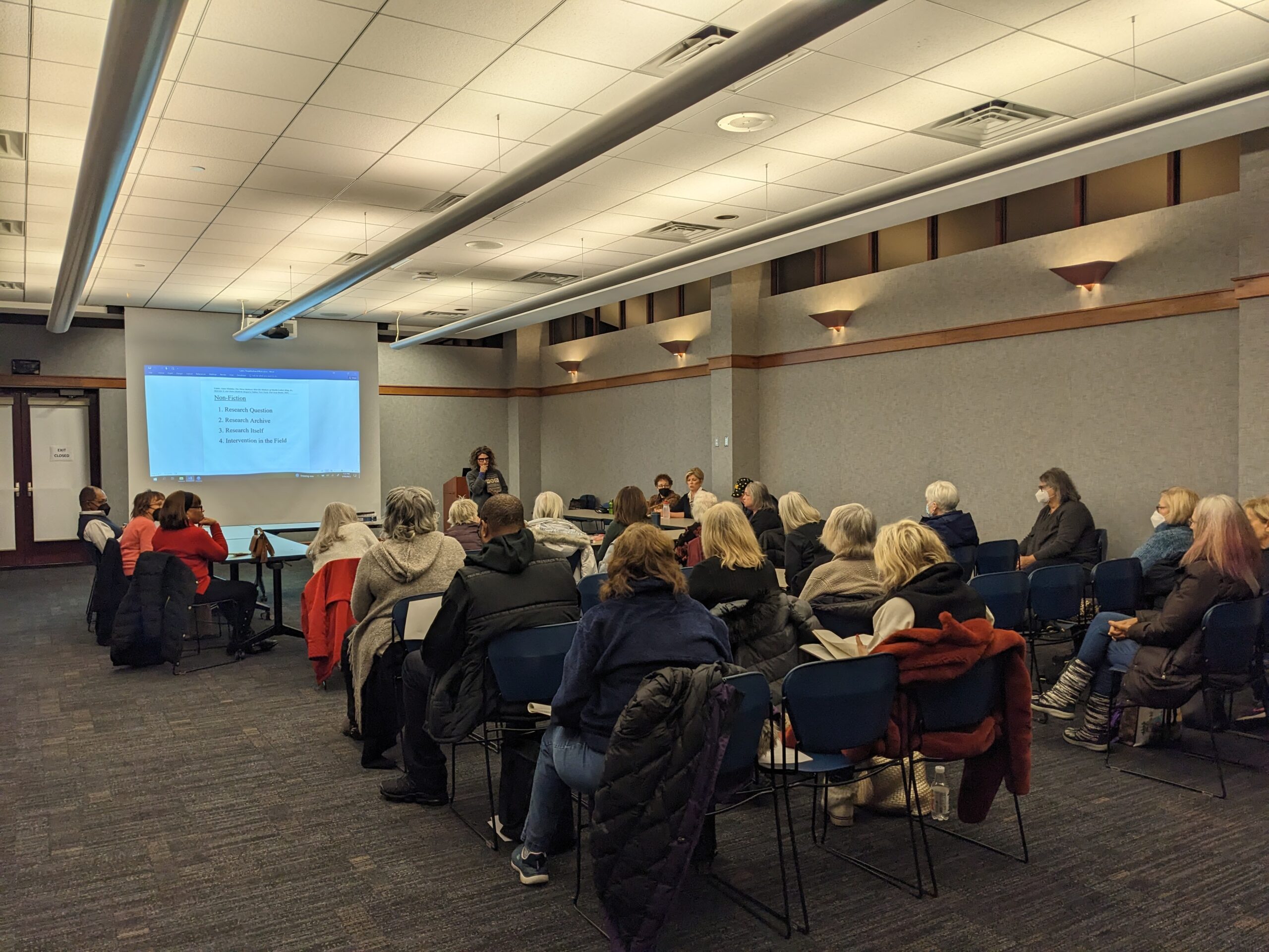 A crowd of people sit watching a presentation.
