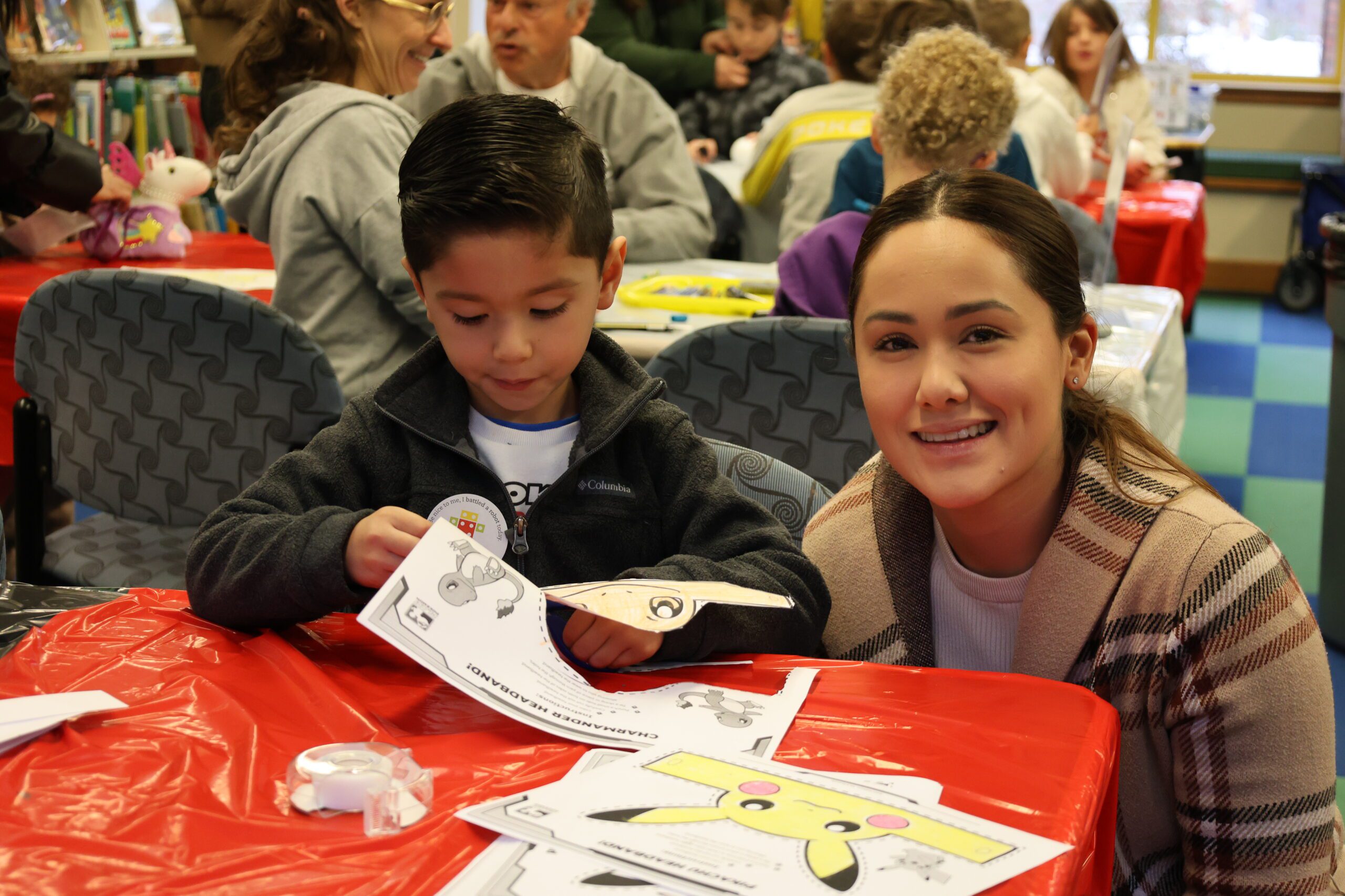 Caregiver smiling at the camera while child cuts paper for a craft
