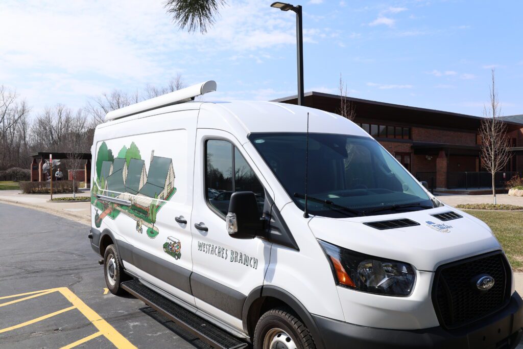 A white Ford Transit with an illustration of the Westacres Branch Library on the passenger's side