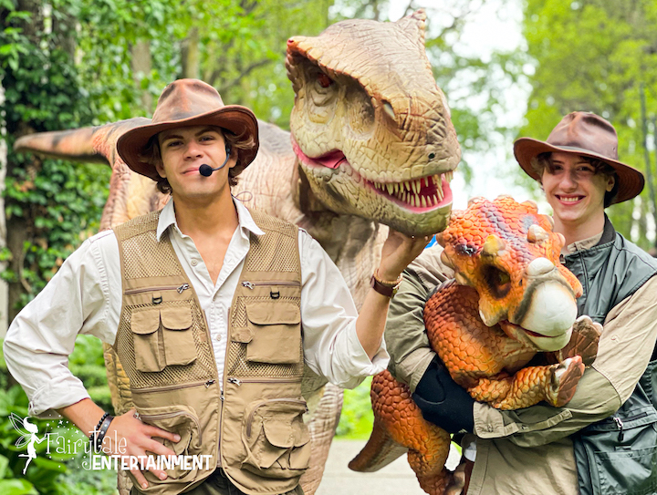 Two adults dressed as zookeepers with a t-rex as big as big as one adult and a baby triceratops.